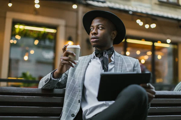 Homme africain assis sur un banc avec tablette et boire du café — Photo