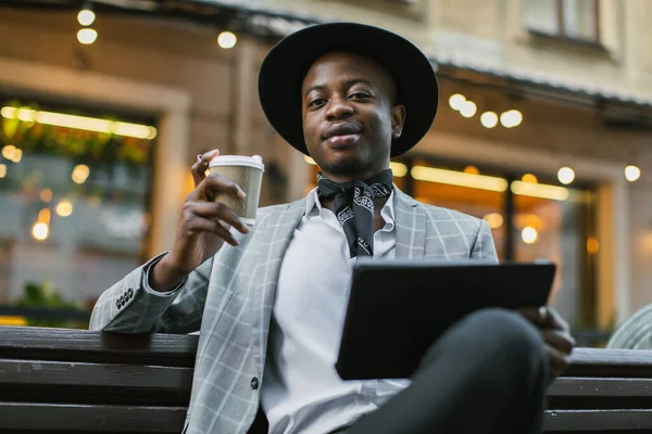 Élégant homme africain assis sur le banc avec café et tablette — Photo