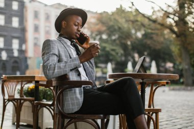 Afrikalı adam cep telefonundan konuşuyor ve kafede kahve içiyor.