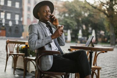 Afrikalı adam cep telefonundan konuşuyor ve kafede kahve içiyor.