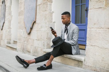 Afrikalı stil sahibi adam sokakta oturuyor ve cep telefonu kullanıyor.