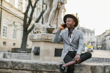 Gülümseyen Afrikalı adam şehir caddesinde cep telefonuyla konuşuyor.