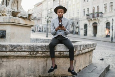 Dışarıda otururken cep telefonundan mesaj atan mutlu Afrikalı adam.