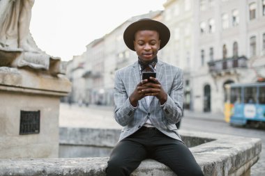 Dışarıda otururken cep telefonundan mesaj atan mutlu Afrikalı adam.
