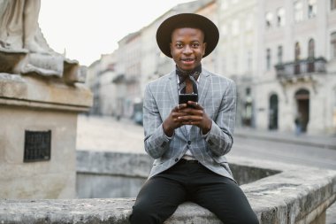 Dışarıda otururken cep telefonundan mesaj atan mutlu Afrikalı adam.