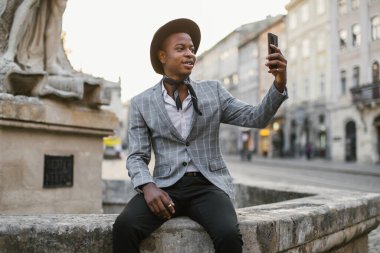 Afro-Amerikalı adam cep telefonuyla dışarıda selfie çekiyor.