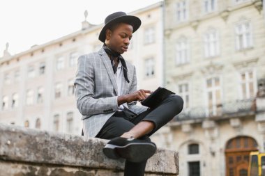 Odaklanmış Afrikalı adam dışarıda oturuyor ve tablet kullanıyor.