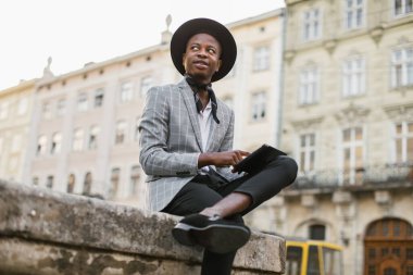 Odaklanmış Afrikalı adam dışarıda oturuyor ve tablet kullanıyor.