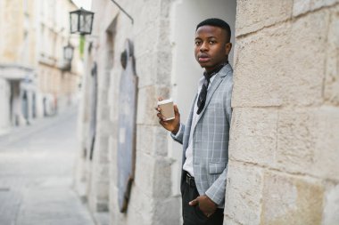 Havalı giyinen düşünceli bir adam dışarıda kahve içerken poz verir.