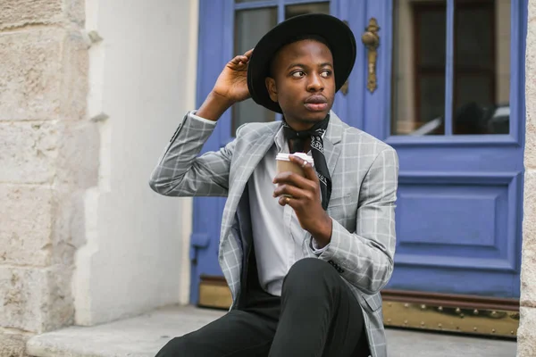 Afrikaanse man in pak zit buiten met een kopje koffie — Stockfoto