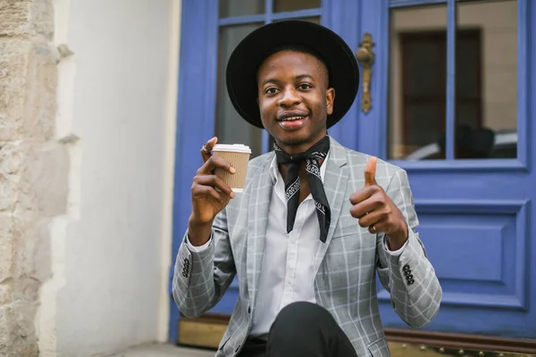 Afrikaanse man in stijlvol pak die buiten koffie drinkt — Stockfoto