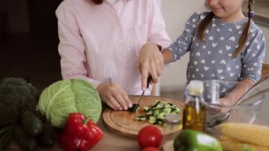 Şirin küçük bir kız ve günlük giysiler içindeki güzel annesi sebze kesiyor.