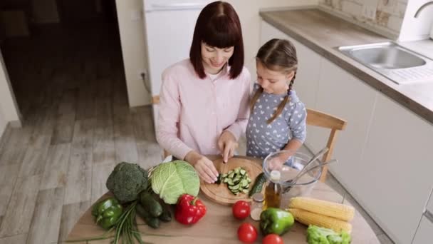 Mãe branca ensinar pouco pré-escolar filha cortar legumes preparando salada para o almoço — Vídeo de Stock