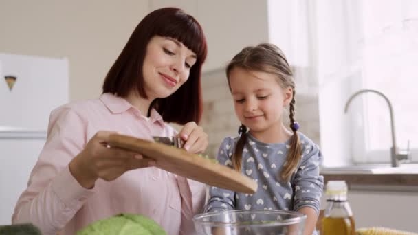 Carino figlia preparare il pranzo con mamma caucasica gettando affettato cipolla in ciotola di vetro — Video Stock