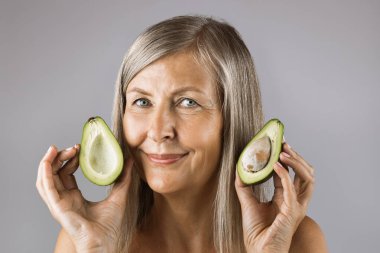 Avokado tutan sağlıklı pürüzsüz derili yaşlı bir kadın.