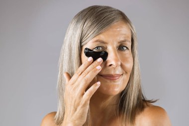 Gözlerinin altında hidrojel bantları olan yaşlı bir kadının portresi.