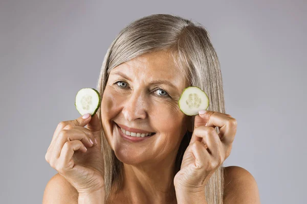 Sonriente anciana sosteniendo rebanadas de pepino orgánico en el interior — Foto de Stock