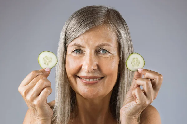 Sonriente anciana sosteniendo rebanadas de pepino orgánico en el interior — Foto de Stock