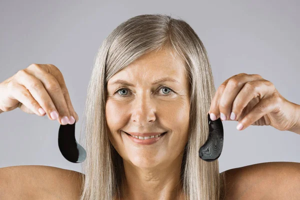 Pleasant woman with aged skin holding black eye patches — Stock Photo, Image