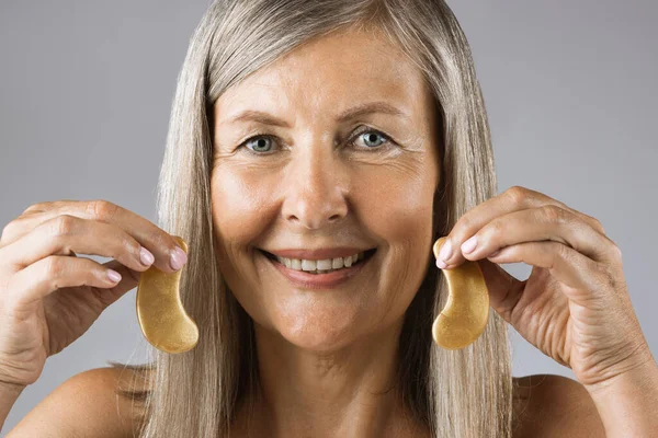 Aged woman holding golden collagen eye patches — Stock Photo, Image