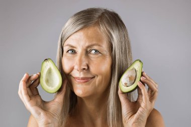 Avokado tutan sağlıklı pürüzsüz derili yaşlı bir kadın.