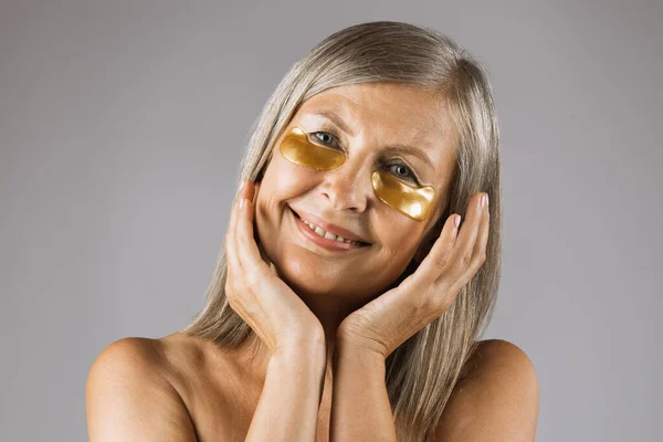 Старшая женщина улыбается на камеру с гидрогелевыми повязками на глазу — стоковое фото