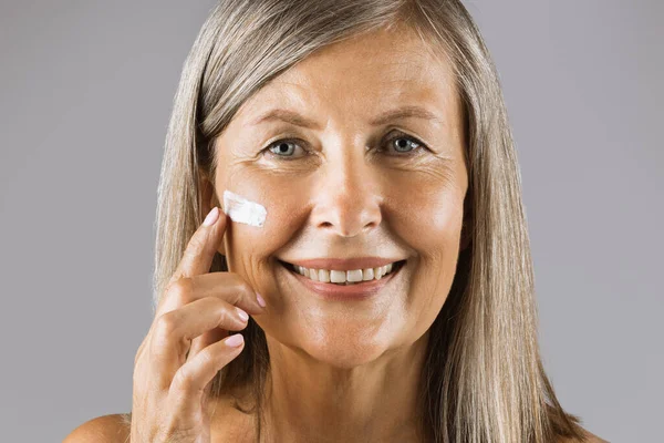 Senior lady smiling and looking at camera with cream on face — Stock Photo, Image