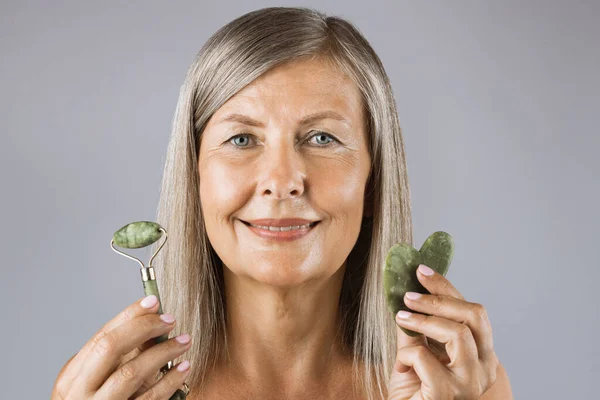 Portrait of aged lady holding jade roller and stone in hands — Stock Photo, Image
