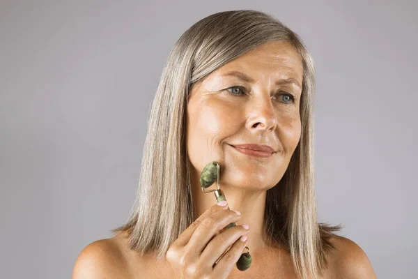 Pretty aged woman massaging face with jade roller — Stock Photo, Image