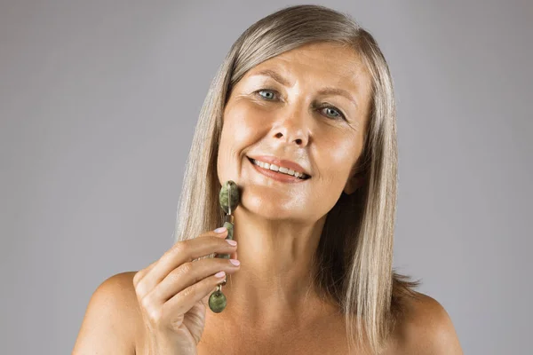 Pretty aged woman massaging face with jade roller — Stock Photo, Image
