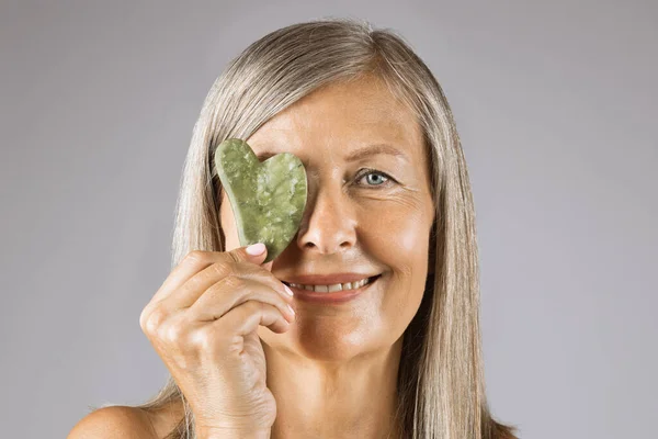 Mature lady covering one eye with jade gua sha stone — Stock Photo, Image