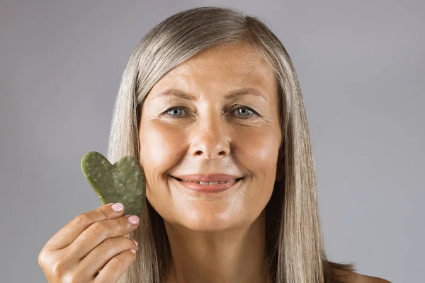 Charming aged woman holding jade gua sha stone — Stock Photo, Image