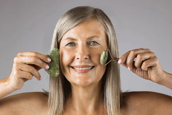 Mature woman holding gua sha massage tools in studio — Stock Photo, Image