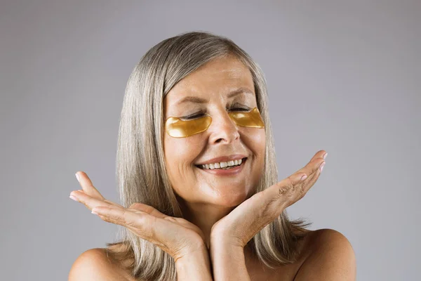 Smiling aged woman using cosmetic patches under eyes — Stock Photo, Image