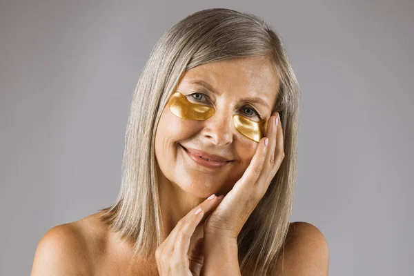 Adorable mature woman using collagen eye patches in studio — Stock Photo, Image