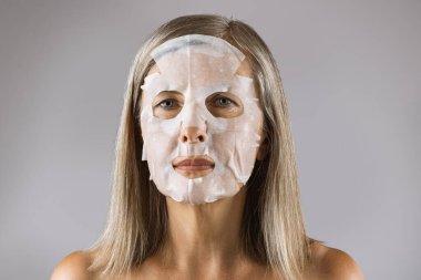 Stüdyoda poz veren yüzü pamuk maskeli yaşlı bir kadın.