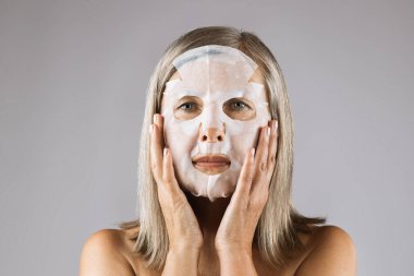 Cilt bakımı için pamuk yüz maskesi kullanan yaşlı bir kadın.