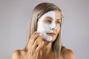 Stüdyoda maskeli yaşlı bir kadın poz veriyor.