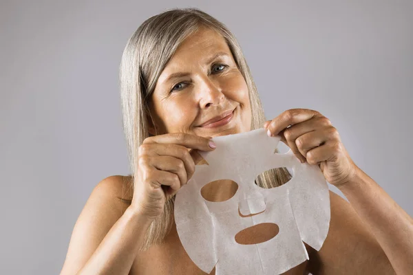 Senior woman smiling on camera with cotton mask in hands — Stock Photo, Image