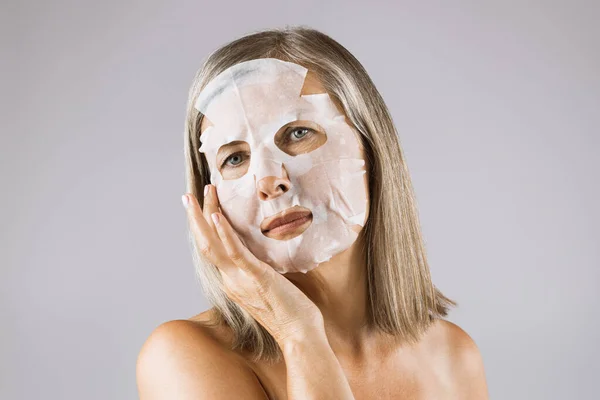 Ohromující starší žena, která aplikuje papírovou masku na obličej — Stock fotografie