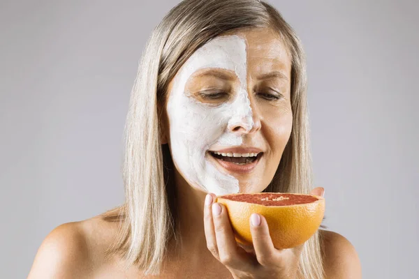 Verouderde vrouw met masker op gezicht met plak grapefruit — Stockfoto