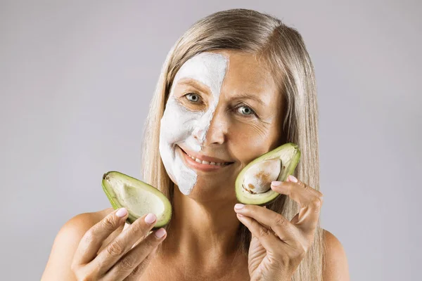 Senior woman holding avocado near her face with mask — Stock Photo, Image