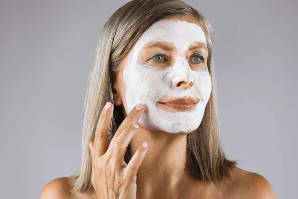Ενηλίκων γυναίκα που εφαρμόζει λευκή καλλυντική μάσκα στο πρόσωπο — Φωτογραφία Αρχείου