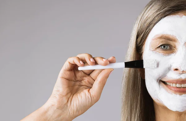 Polovina obličeje dospělé ženy pomocí štětce pro aplikaci masky — Stock fotografie