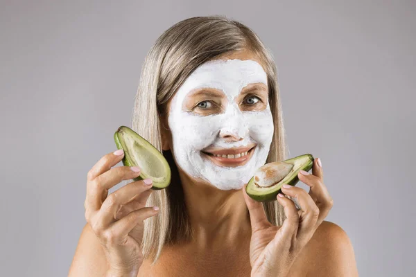Kobieta z maską twarzy w studio trzyma połówki awokado — Zdjęcie stockowe