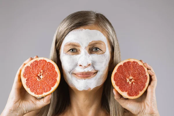 Érett nő arcmaszkkal, grépfrútszeleteket tartva — Stock Fotó
