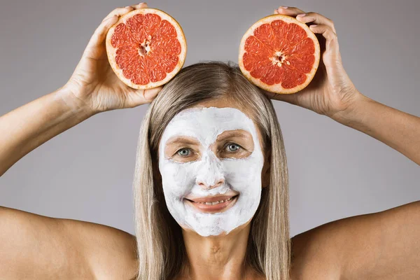 Wanita dewasa dengan topeng kosmetik di wajah memegang jeruk — Stok Foto