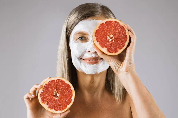 Femme âgée avec masque facial cachant ses yeux sous un pamplemousse tranché — Photo