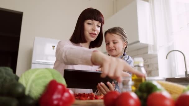 Feliz caucásico joven hija y su joven madre teniendo en línea cocina clase en la tableta — Vídeos de Stock