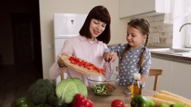 Zblízka roztomilé dcery připravit oběd s kavkazskou maminkou házení nakrájený pepř — Stock video